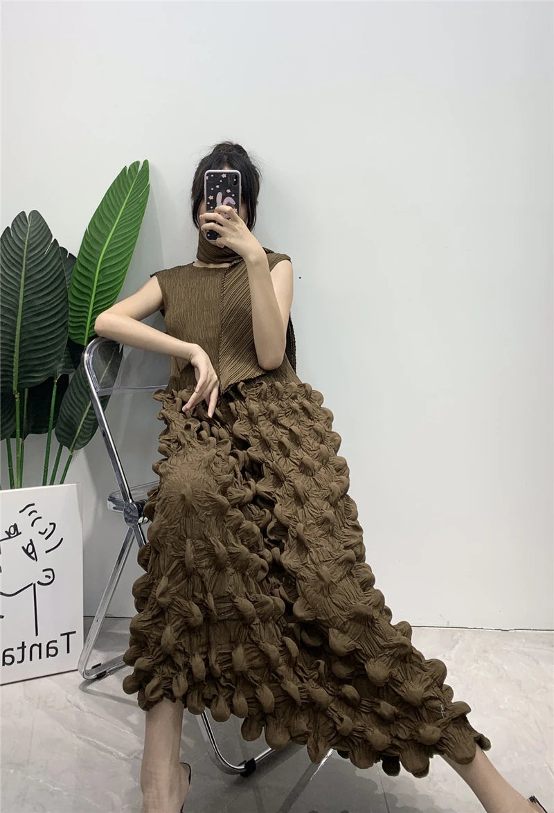 Woman wearing a brown textured dress standing against a white wall with a plant to the left.