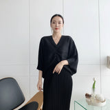 Person wearing a black outfit taking a mirror selfie in a minimalistic room.
