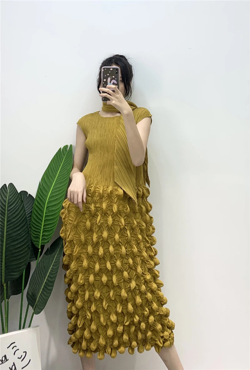 Person wearing a mustard yellow textured dress against a white wall with green leaves.