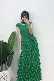 Person wearing a green dress with textured pattern against a white wall.