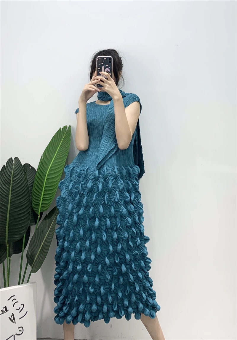 Person wearing a blue textured dress against a white wall with green leaves.