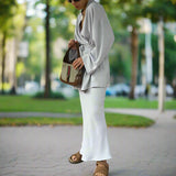 Woman in a light gray outfit holding a patterned handbag, standing on a wooden deck.