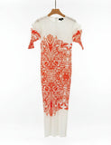 White dress with red floral pattern on a hanger against a background of shelves with folded clothes.