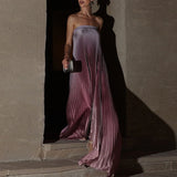 Woman in a long, flowing purple dress standing against a textured wall.
