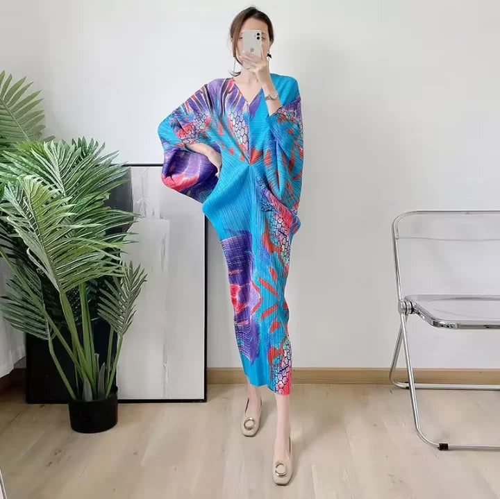 Person wearing a colorful kimono-style garment in a room with a plant and chair.