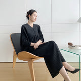 Person wearing a black outfit sitting on a chair in a minimalistic room.