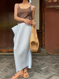 Person wearing a brown tank top and white skirt holding a beige bag on a herringbone floor.