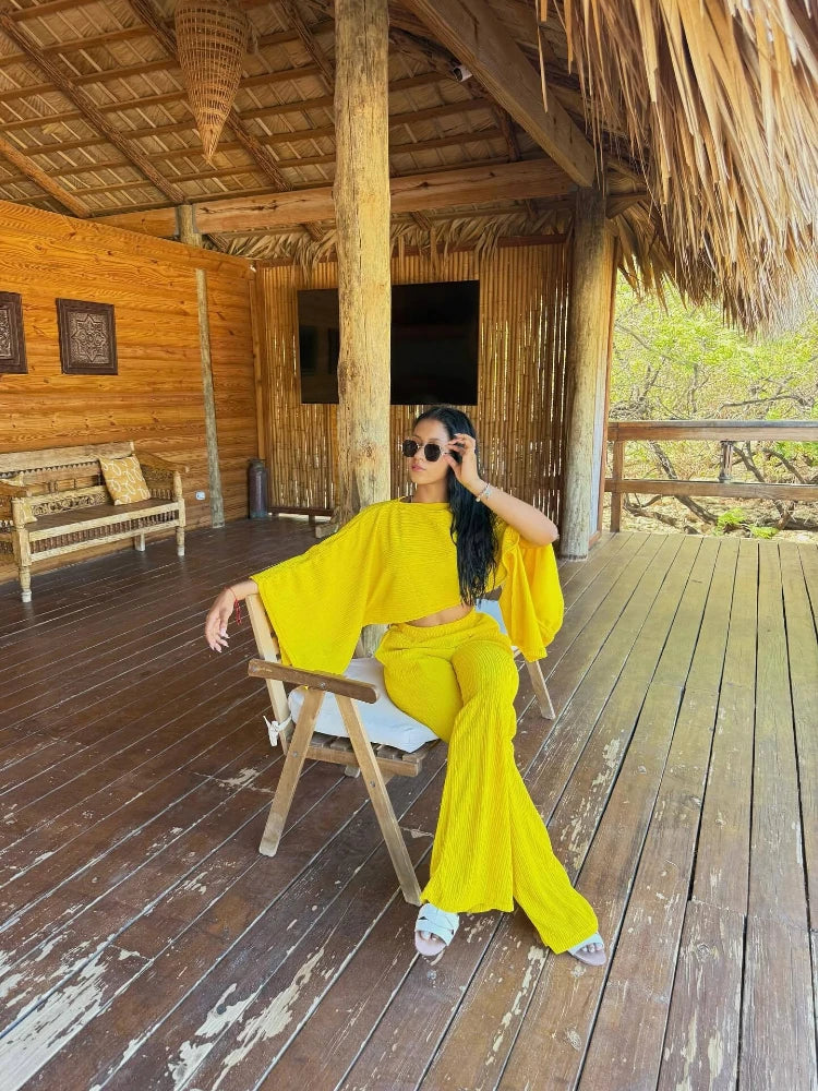 Woman in a yellow outfit sitting on a wooden chair in a rustic setting.