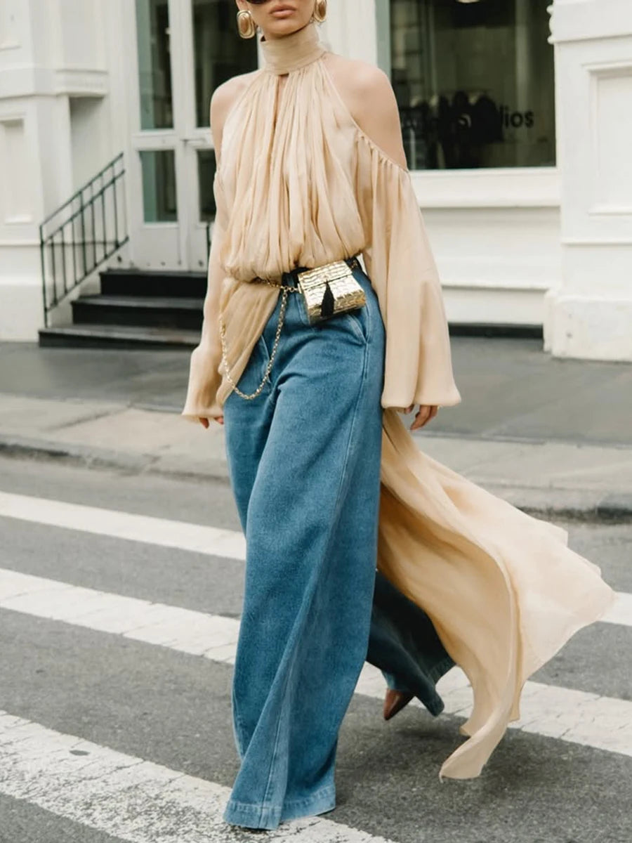 Person wearing a beige top and blue jeans walking on a street.