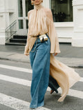 Person wearing a beige top and blue jeans walking on a street.