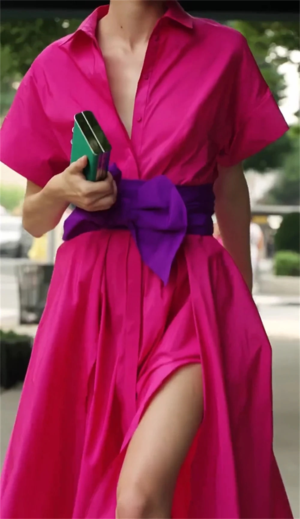 Person wearing a bright pink dress with a purple belt in an outdoor setting
