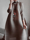 Person wearing a long, light brown dress with a decorative heart pendant on a neutral background