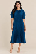 A blue pleated midi dress with short sleeves and a round neckline, hanging on a white hanger against a textured beige wall.