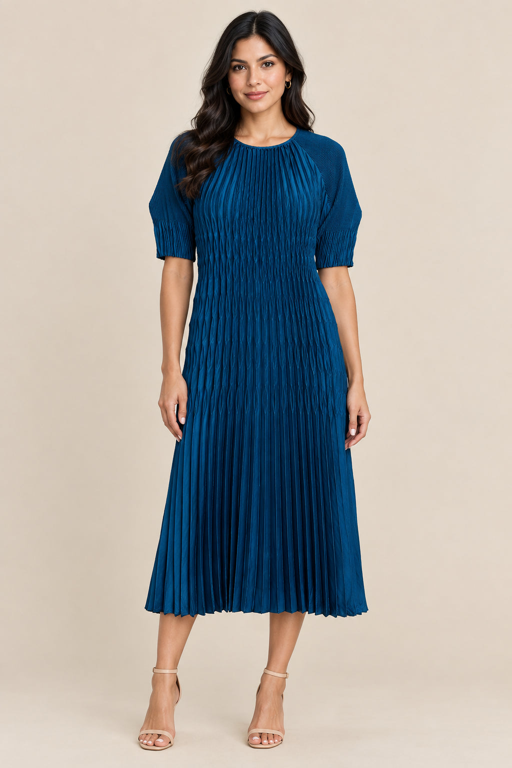 A blue pleated midi dress with short sleeves and a round neckline, hanging on a white hanger against a textured beige wall.