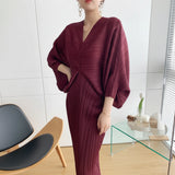 Person wearing a burgundy outfit taking a mirror selfie in a modern room.
