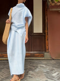 Person wearing a light blue traditional outfit with a straw bag in front of a wooden door.