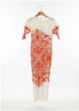 White dress with red floral pattern on a hanger in front of a shelf with folded clothes.