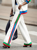 Person wearing white pants with colorful stripes walking outdoors.