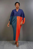 Woman wearing a blue and orange dress holding a beige bag against a gray background
