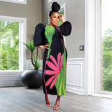 Woman in a colorful dress standing in a room with large windows and a plant.