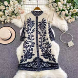 Embroidered dress with floral patterns on a textured surface with flowers and a hat in the background