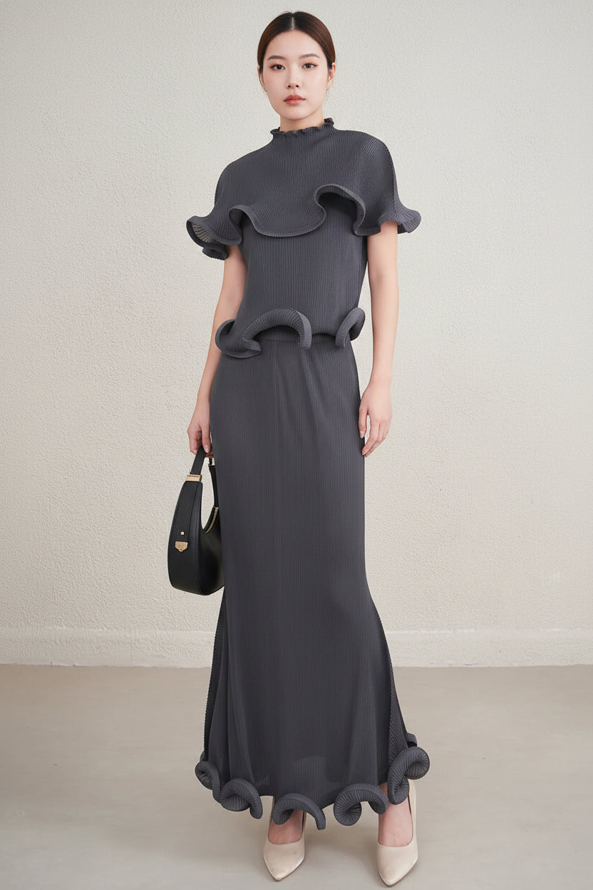 Woman wearing a long dark gray dress with ruffled details on a plain background