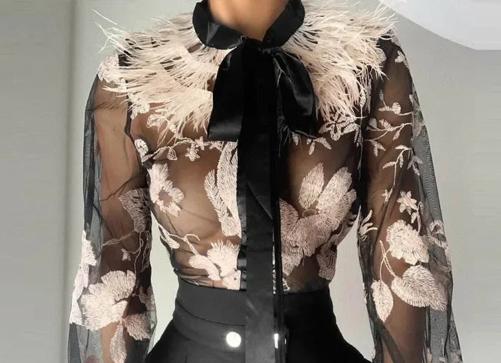 Sheer floral blouse with black ribbon and black pants on a plain background