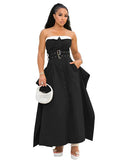 Woman wearing a black strapless dress with a belt, holding a white handbag on a white background.