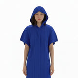 Person wearing a blue pleated dress taking a mirror selfie with colorful clothing in the background.