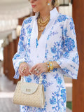 Woman wearing a blue and white floral dress with gold accessories, holding a beige handbag.