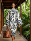 Woman in a patterned dress holding a brown bag, standing on a wooden path with greenery in the background