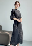 Person wearing a black dress with a chevron pattern in a minimal indoor setting.