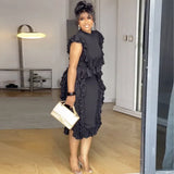 Woman in a black ruffled dress holding a white clutch in an indoor setting.