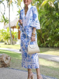 Woman in a blue floral dress standing outdoors with greenery in the background