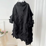 Black textured poncho on a hanger against a white curtain background