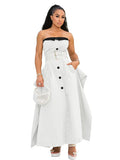 Woman wearing a white strapless dress with black buttons, holding a white handbag on a white background.