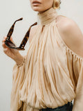 Woman wearing a beige off-shoulder top holding sunglasses against a neutral background