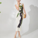 Woman wearing a white dress with green and black floral pattern on a plain background