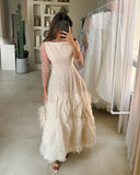 Woman taking a mirror selfie wearing a long, light-colored dress with feather details.