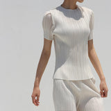 Person wearing a white pleated outfit against a light gray background