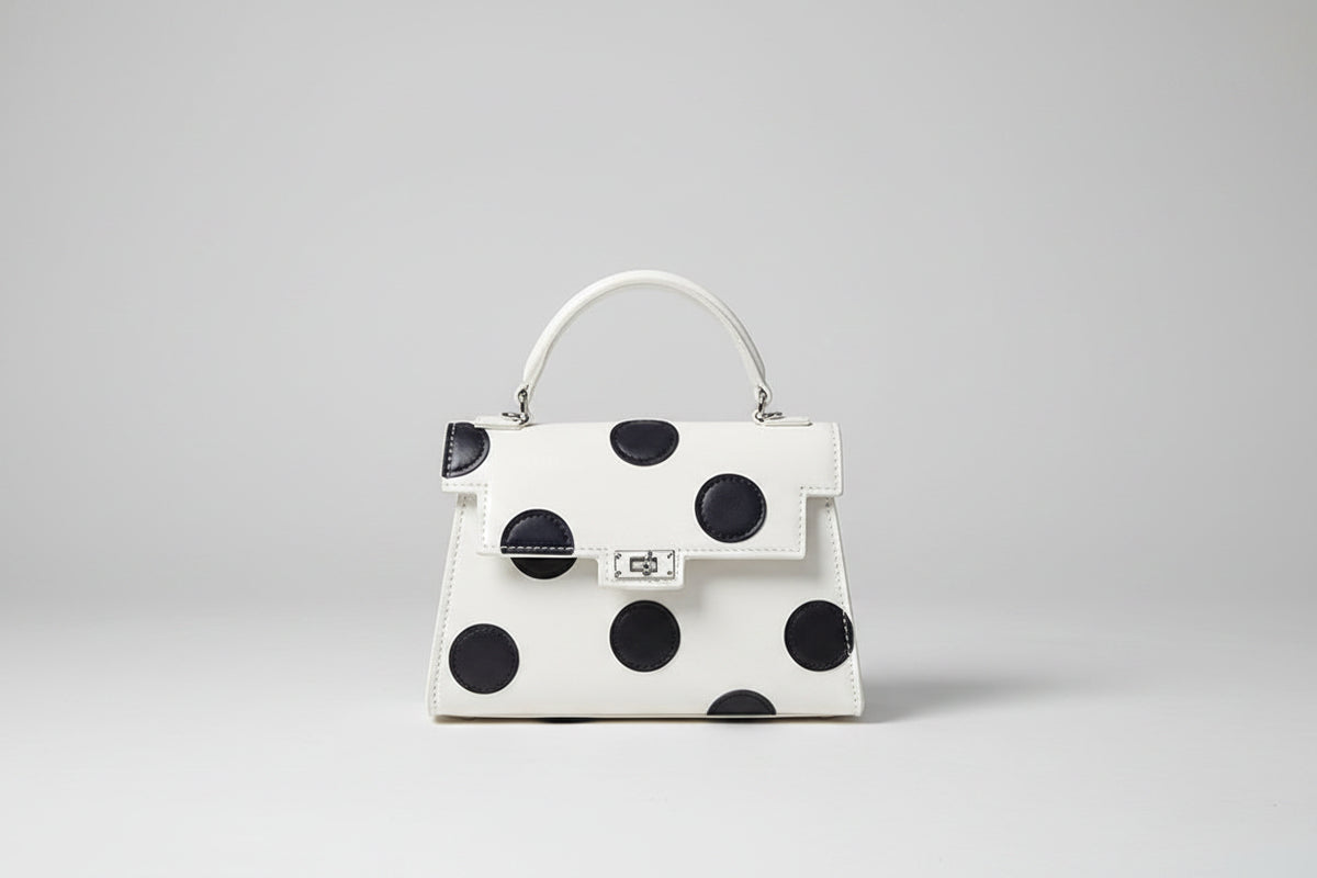 White handbag with black polka dots on a beige surface with a pinkish-brown background