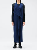Person wearing a long blue pleated dress over a black top on a white background