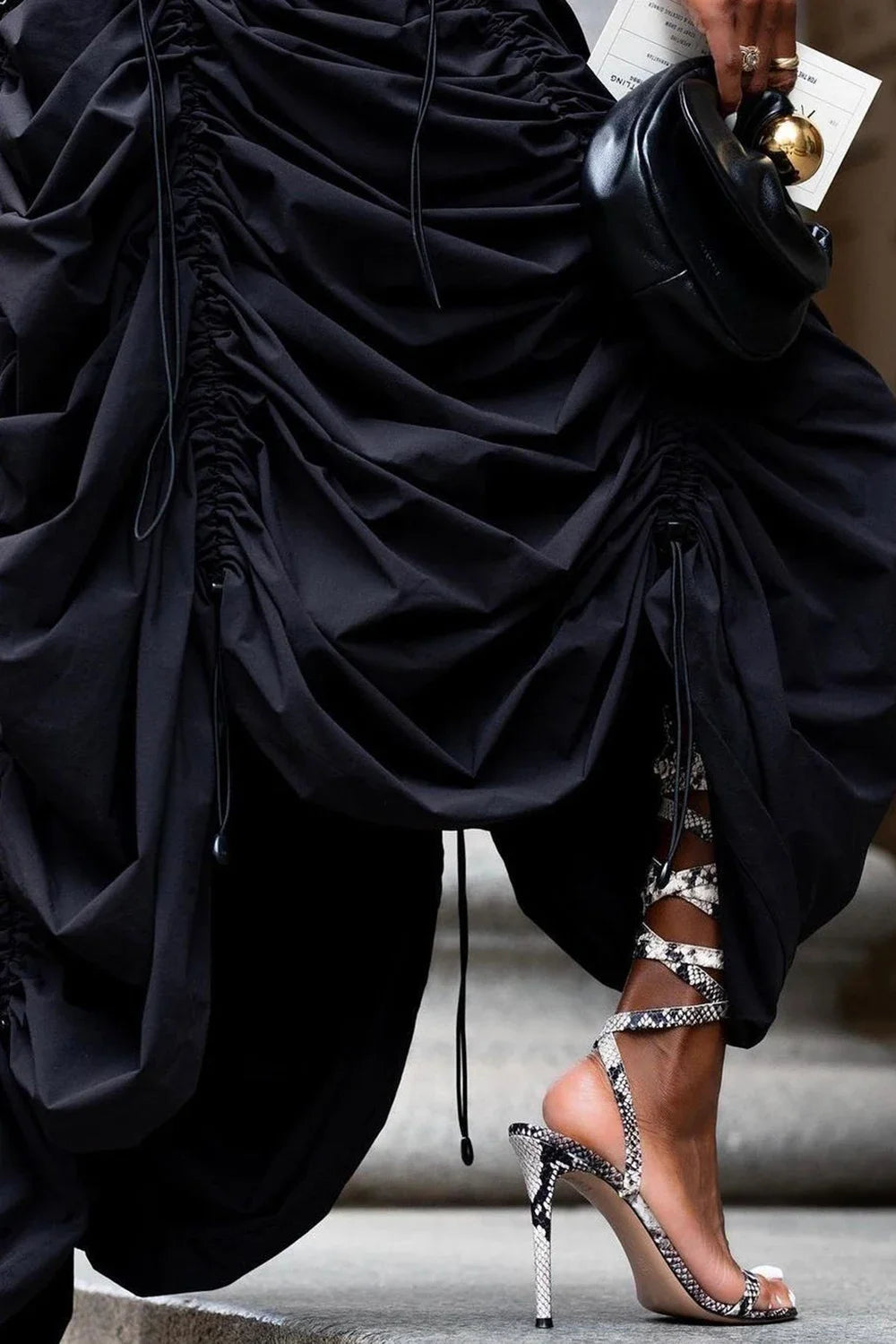 Person wearing a black ruched dress with high-heeled sandals on a blurred background