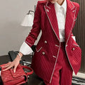Person wearing a red pinstripe suit holding a red handbag indoors.