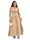 Woman wearing a beige strapless dress with buttons holding a white handbag on a white background.