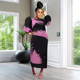 Woman in a black and pink dress standing in a room with large windows and a plant.