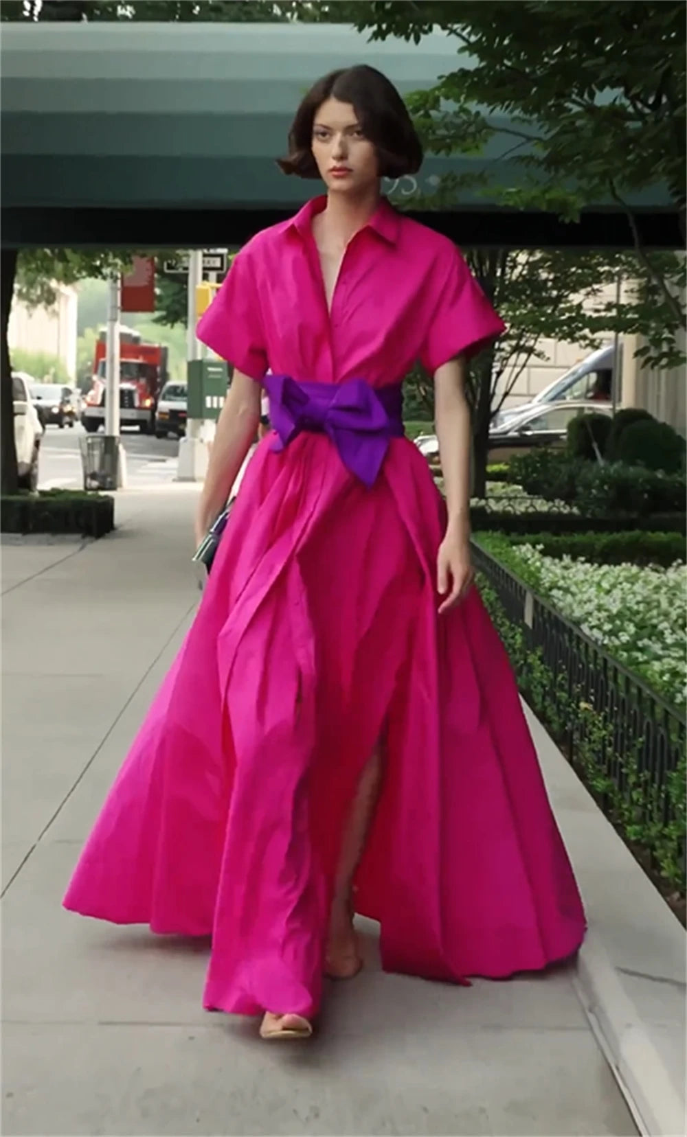 Woman wearing a bright pink dress with a purple belt on a city street.