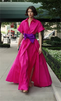 Woman wearing a bright pink dress with a purple belt on a city street.