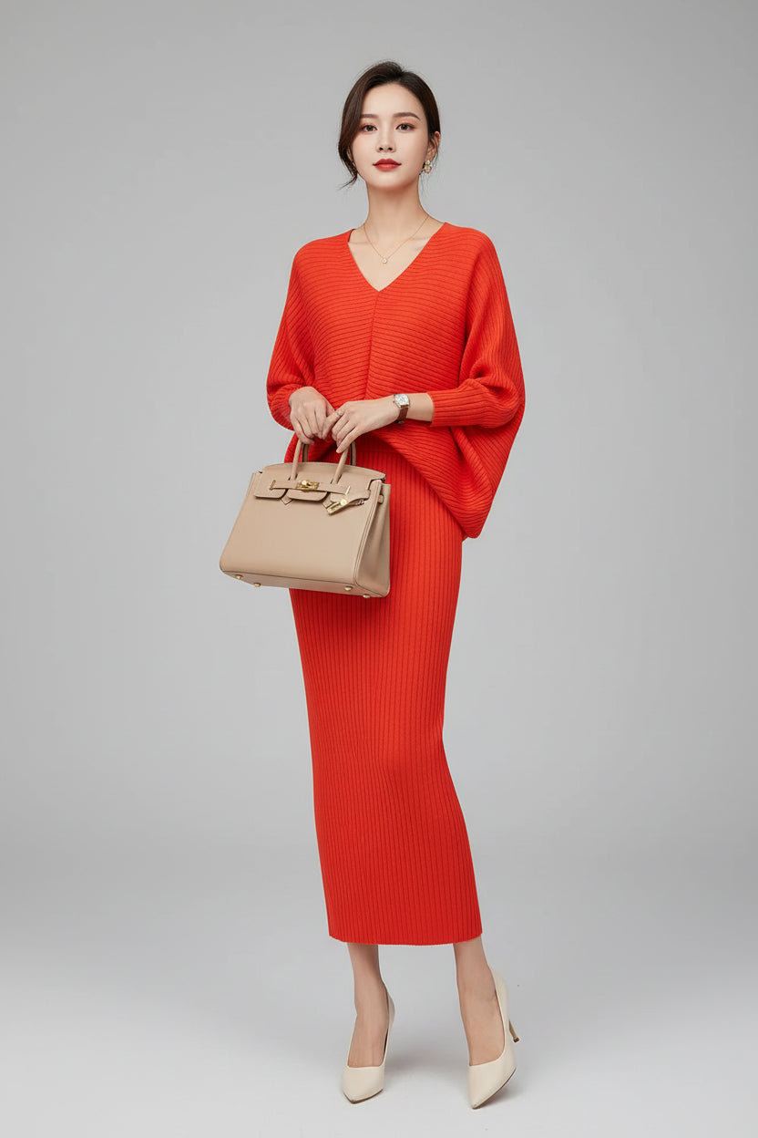 Person wearing a bright red dress holding a beige handbag against a dark wall.