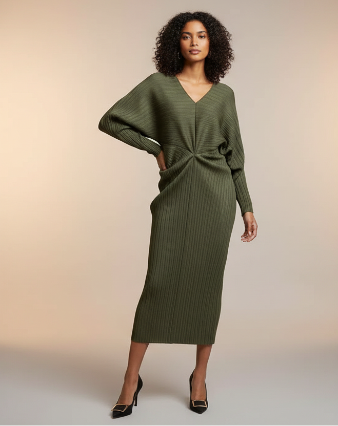Person wearing a green ribbed dress against a gray wall.